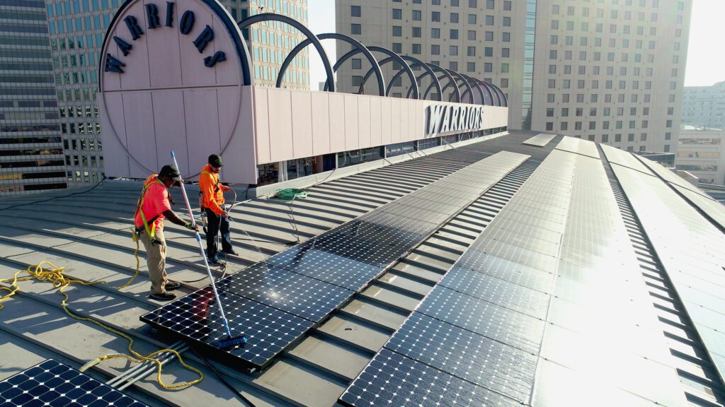 2 men from Synergy Power cleaning off the solar panels at the Golden State Warriors arena