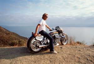 Arlen Ness sitting on a custom built motorcycle on the pacific coast